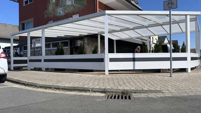 Blick auf ein modernes, überdachtes Sitzbereich mit weißen Wänden und Pflanzen.