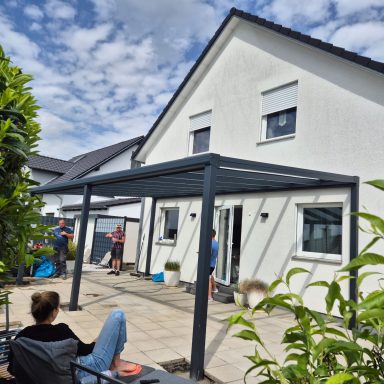 Familie versammelt sich unter einem modernen Terrassendach vor einem weißen Haus.