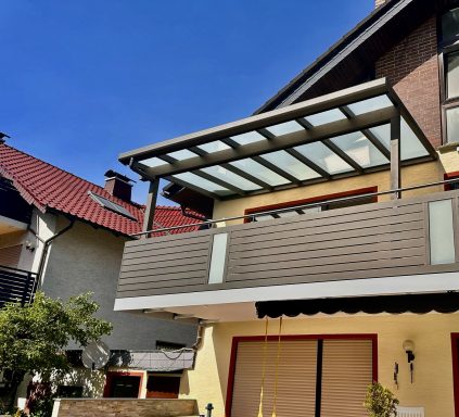 Modernes Haus mit Balkon und Glasüberdachung, blauer Himmel im Hintergrund.
