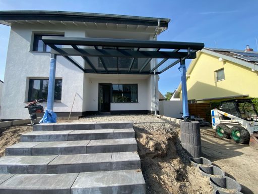 Modernes Haus mit überdachter Terrasse und gestuften Steinen im Vordergrund.